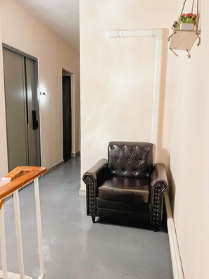 A hallway with a black leather armchair, a wooden table, and a white radiator. - Moochi Relax Lassommoir (Bangkok)