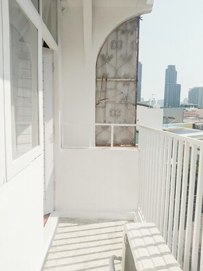 A balcony with a white railing, a window with decorative metal bars, and a view of a cityscape with tall buildings. - Moochi Relax Lassommoir (Bangkok)