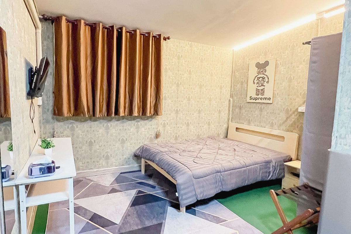 A bedroom with a bed, a desk, a chair, and a wall-mounted picture.