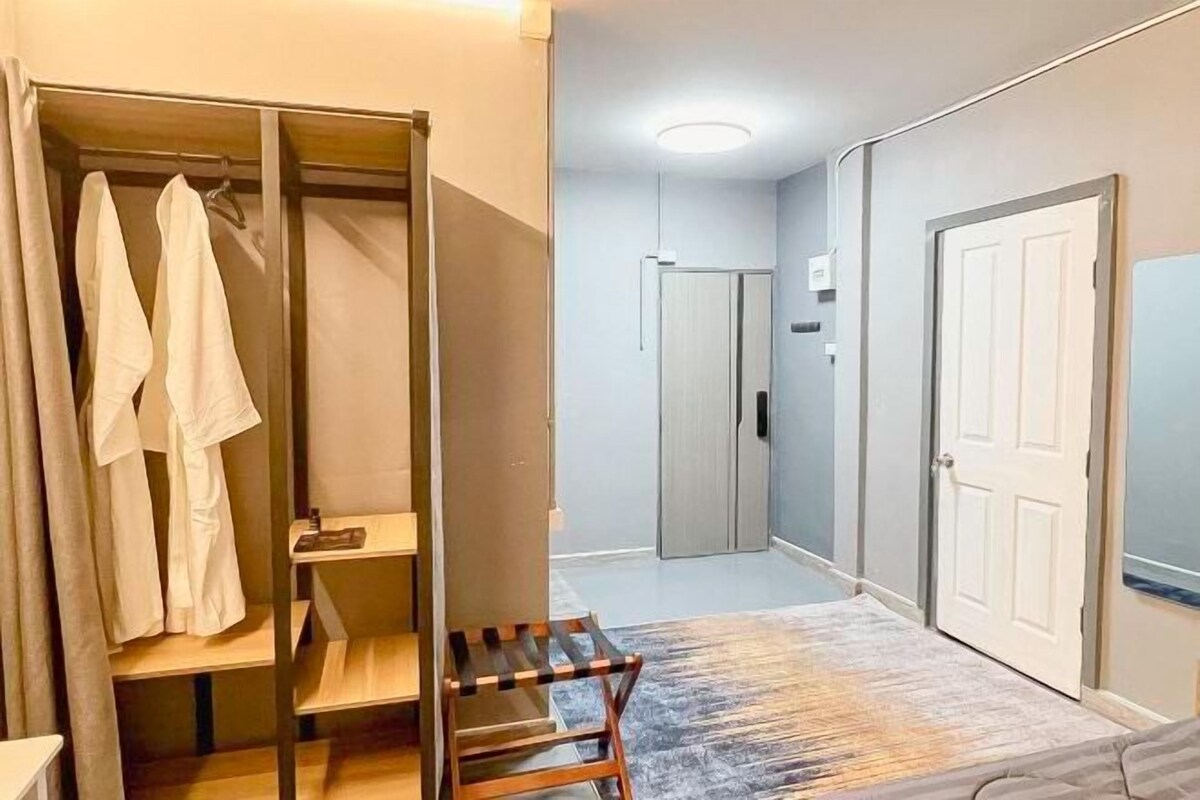 Habitación de hotel con vestidor, un pequeño banco de madera, alfombra estampada y puerta que da a otra habitación.