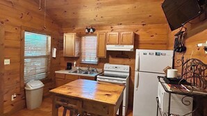 A wooden cabin kitchen with a central island, a stove, refrigerator, and a ceiling fan. - Cozy cabin on the water (Jasper)