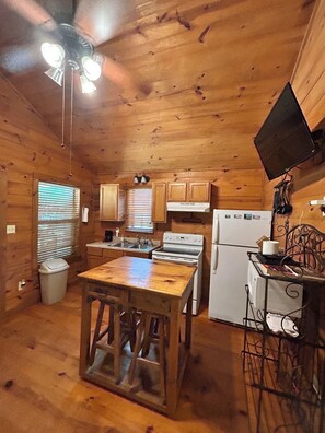 A wooden cabin kitchen with a central island, a stove, refrigerator, and a ceiling fan.