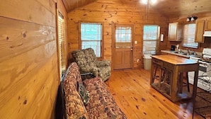 A cozy cabin interior with a sofa, two armchairs, a dining table, and a kitchen area. - Cozy cabin on the water (Jasper)