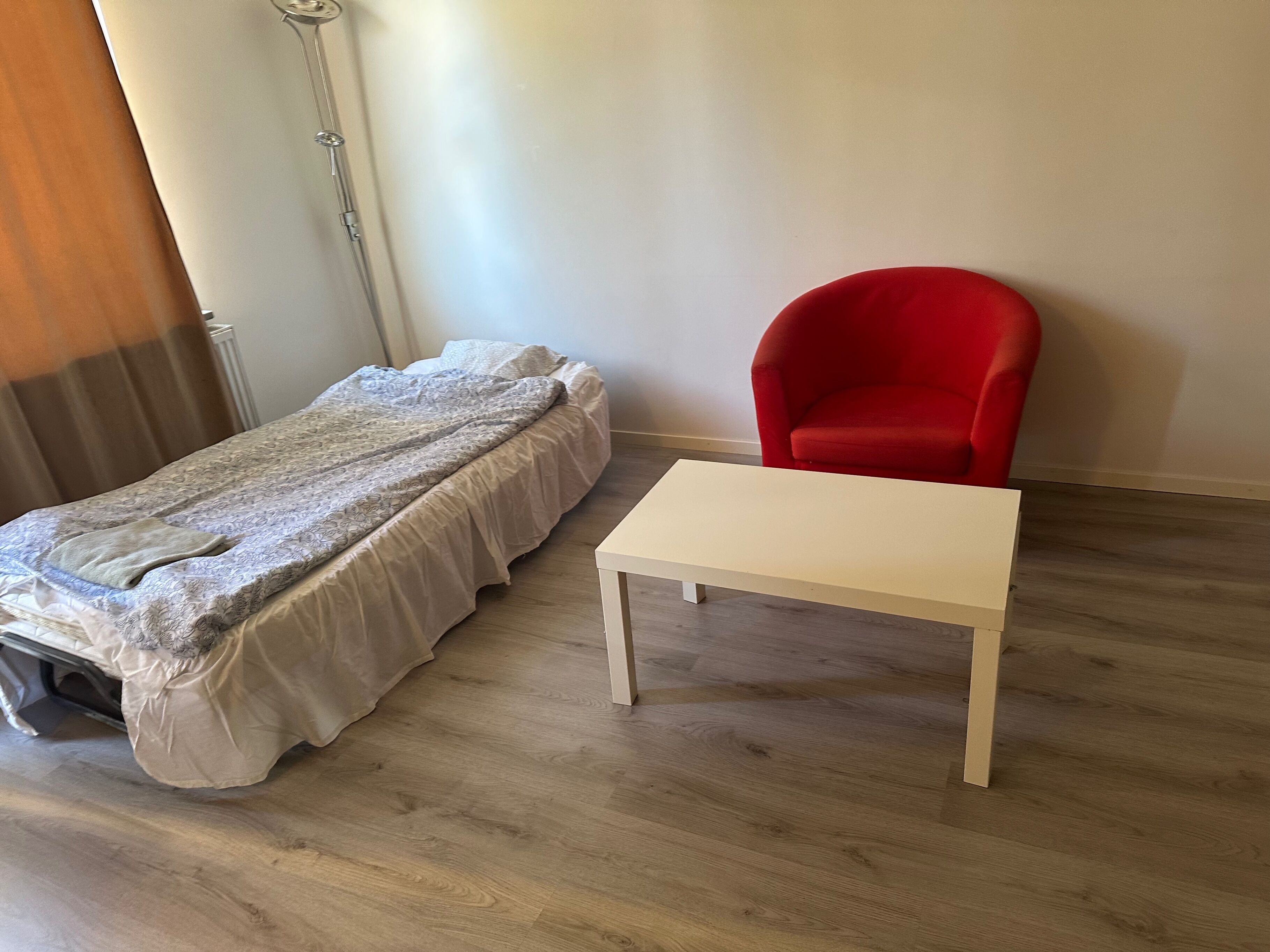 Ein Zimmer mit einem Bett, einem roten Sessel und einem kleinen weißen Tisch.