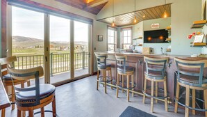 A bar area with wooden stools, a bar counter, and a large TV screen. - Hot Tub & Mtn Views: Townhome in Granby! (Granby)