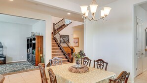 A dining area with a table set for four, surrounded by wooden chairs, a chandelier, and a staircase leading to another level. - Rio Bravo Country Club Home in Bakersfield w/ Pool (Bakersfield)