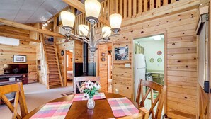 L’intérieur d’un chalet en bois comprend un coin repas avec une table en bois, des chaises et un lustre.