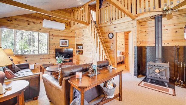 L’intérieur d’une cabane en rondins comprend un salon, une cheminée, un escalier en bois et un téléviseur.