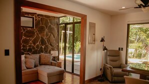 Una sala moderna con una pared de acento de piedra, un sofá modular, un sillón reclinable y vistas a una piscina.
