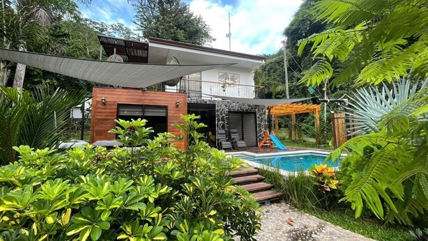 Una casa moderna con piscina, rodeada de exuberante vegetación y una pérgola.