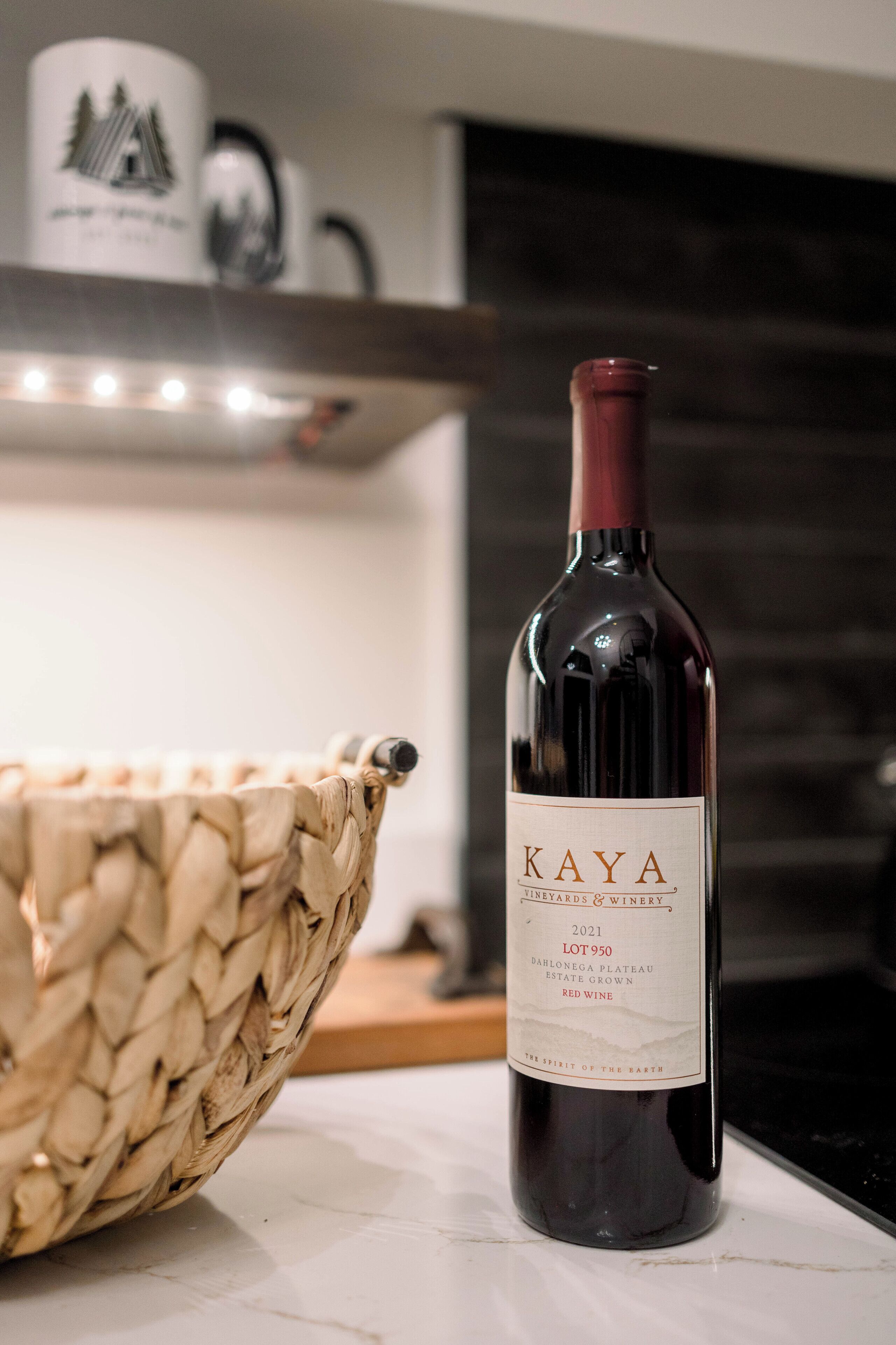 A bottle of 2021 Kaya Lot 950 wine on a marble countertop with a woven basket beside it.