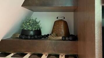Una estantería de madera con un tarro de comida en conserva, una planta en maceta, una campana decorativa y copas de vino.
