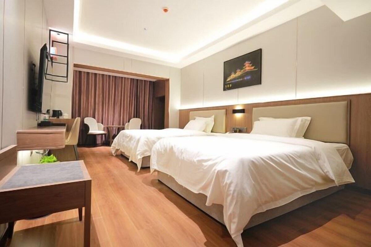 A hotel room with two beds, a desk, a chair, a TV, and a painting on the wall.