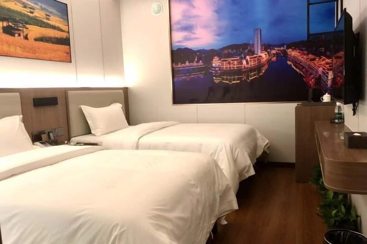 A hotel room with two beds, a wooden desk, and a large cityscape painting on the wall.