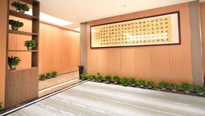 A modern hotel lobby with wooden paneling, a large framed calligraphy piece on the wall, and a row of potted plants along the walkway. - Suining Linhai Hotel (Suining)