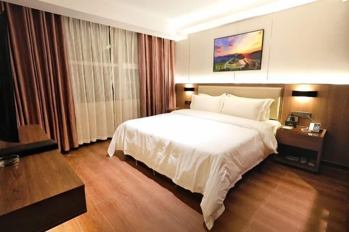 A hotel room with a large bed, a desk, a chair, a nightstand with a lamp, and a painting on the wall.