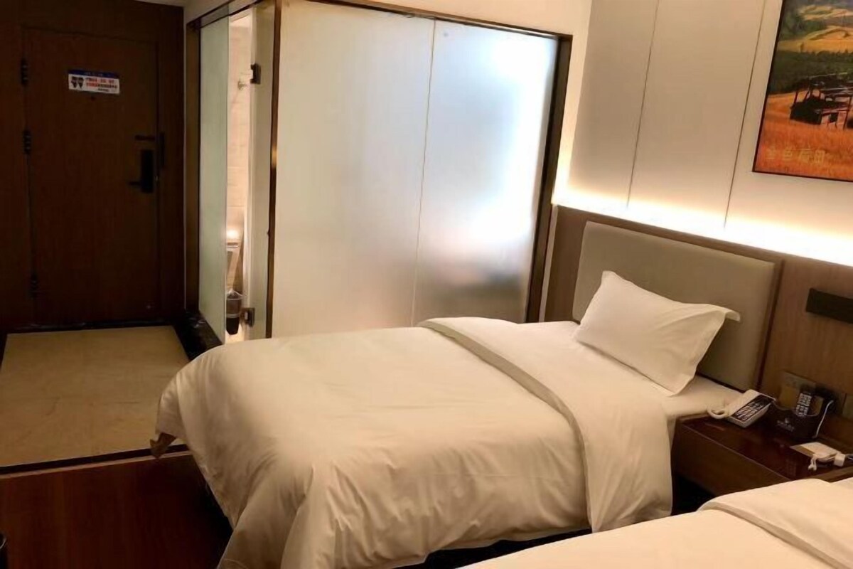 A hotel room with a bed, a nightstand with a phone, and a door with a sign.