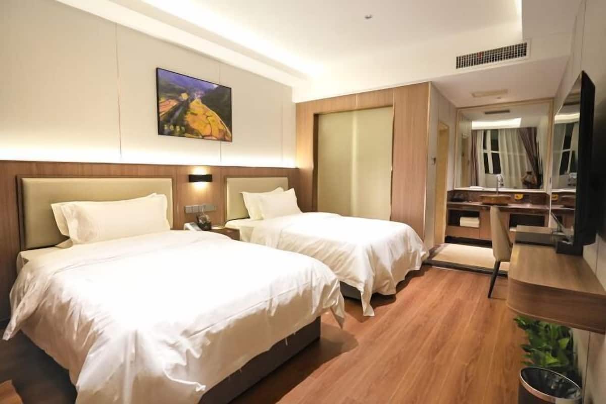 A hotel room with two beds, a desk, a mirror, and a painting on the wall.