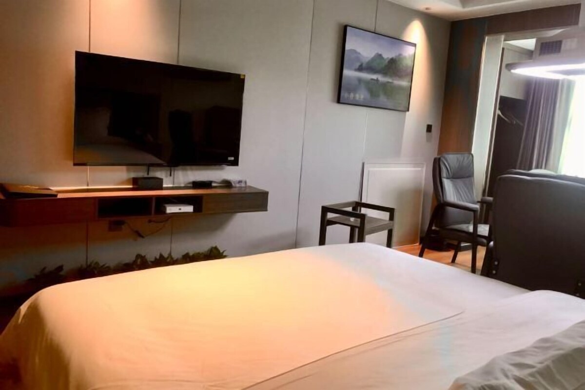A hotel room with a bed, a TV mounted on the wall, a chair, and a painting.