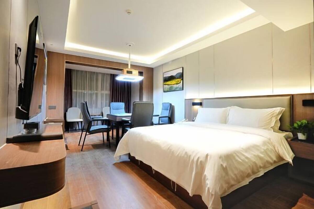 A hotel room with a bed, a desk, chairs, a television, and a painting on the wall.