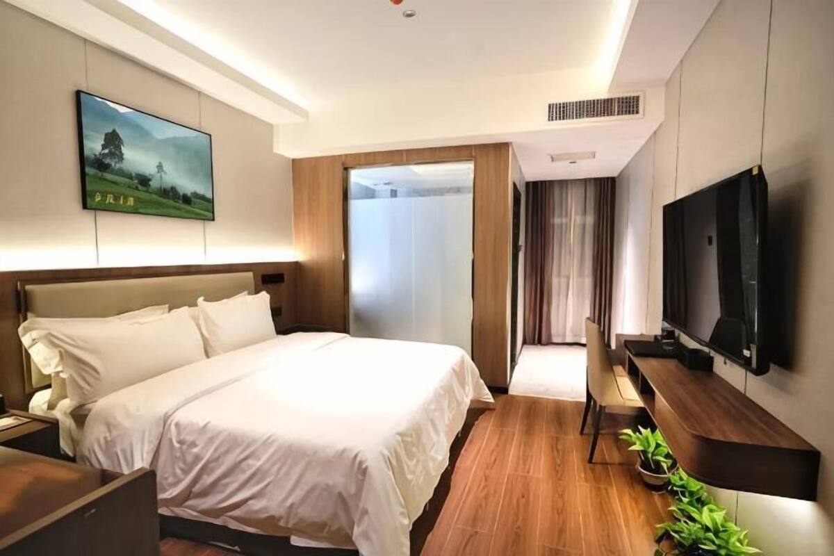 A modern hotel room with a bed, a desk, a television, and a large window.