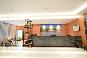 Zona de recepción de un hotel con mostrador, área de asientos y un amplio ventanal con vista a la ciudad.