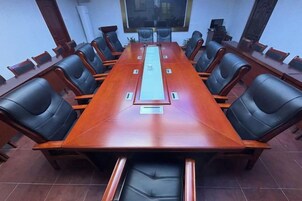 Un salón de conferencias con una larga mesa, sillas negras y una pantalla de proyector.