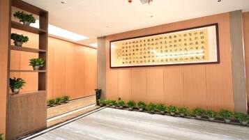 A hallway with a wooden floor, potted plants, and a large framed text on the wall.