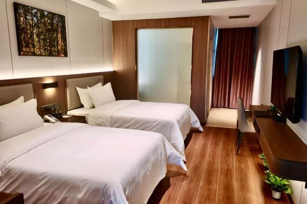 A hotel room with two beds, a TV, a desk, and a large window.