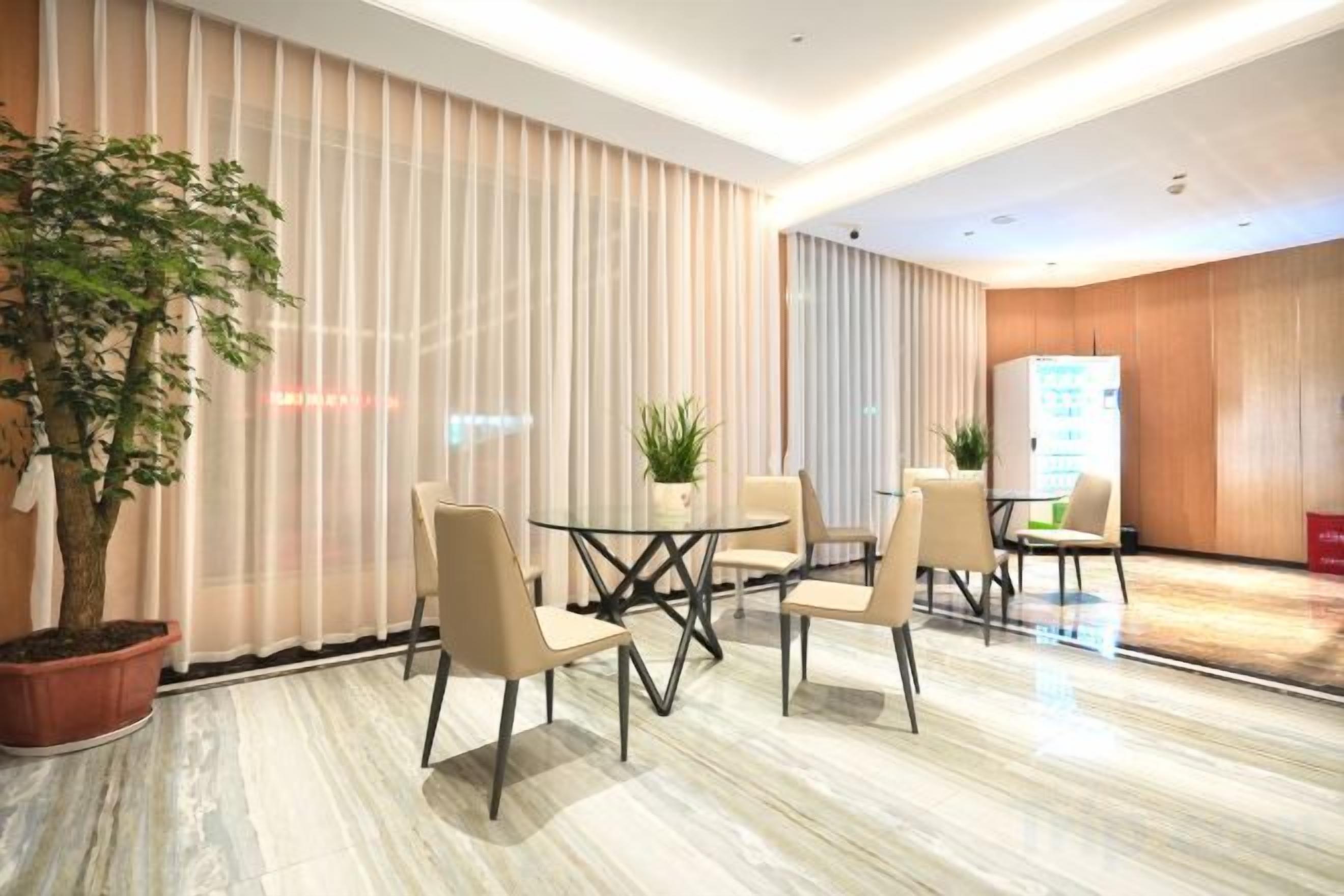 A modern hotel room with a marble floor, a round table with chairs, a potted plant, and a large window with curtains.