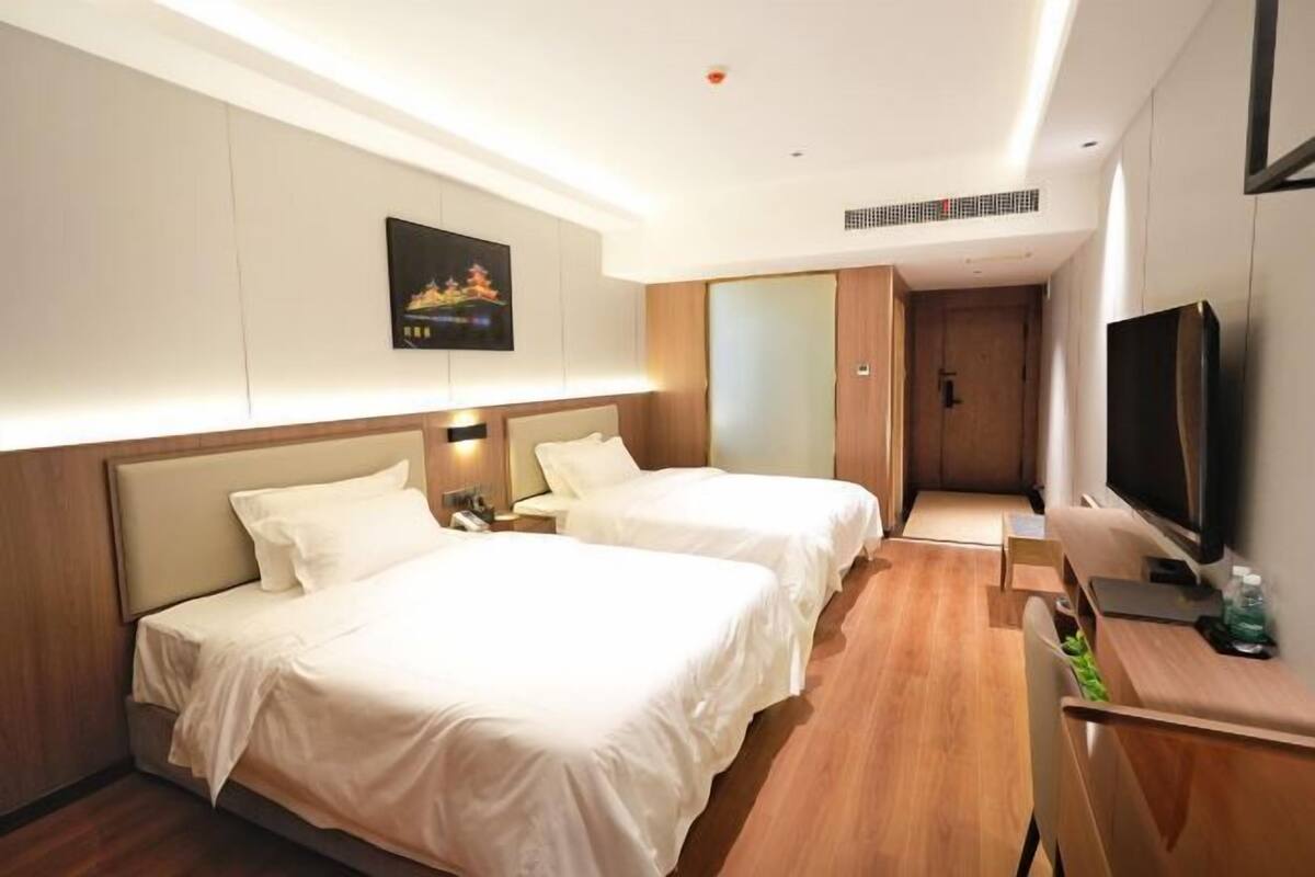 A hotel room with two beds, a TV, a desk, and a painting on the wall.