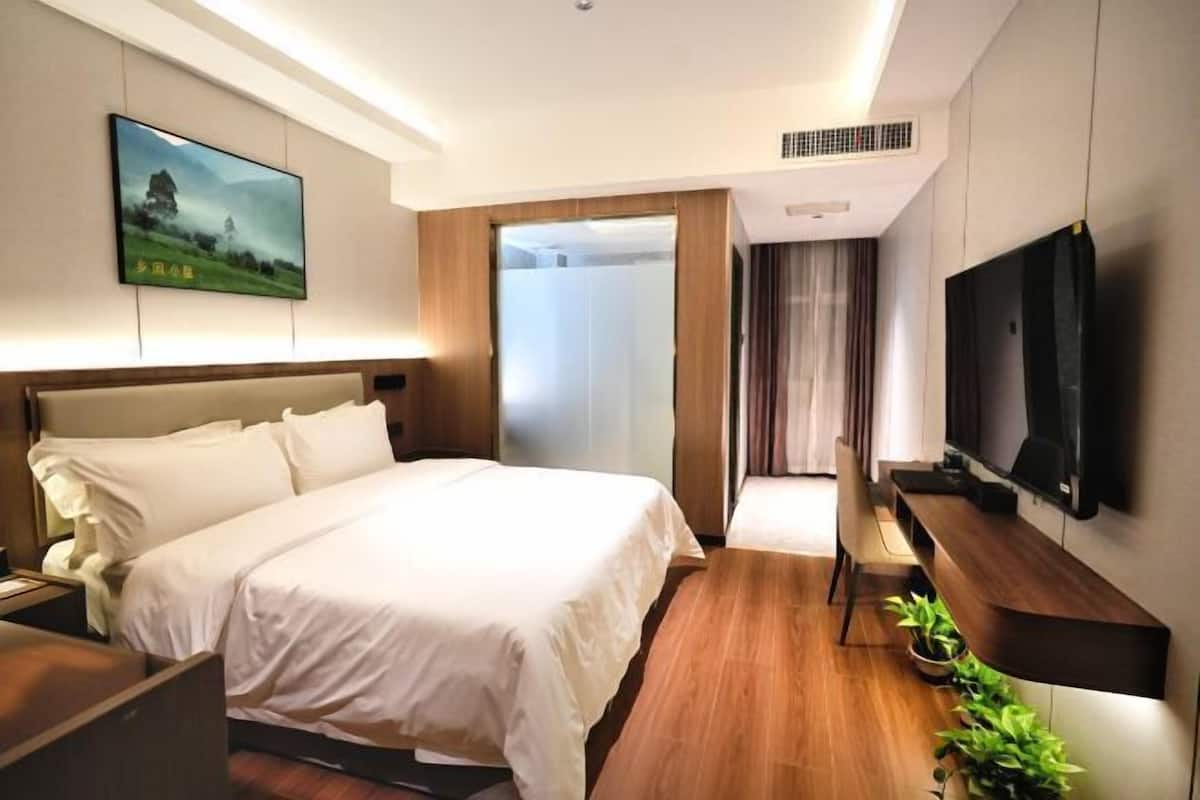 A hotel room with a large bed, a TV, a wooden floor, and a painting on the wall.