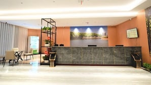 A modern reception area with a marble reception desk, a seating area with chairs, a plant shelf, and a large wall mural. - Suining Linhai Hotel (Suining)