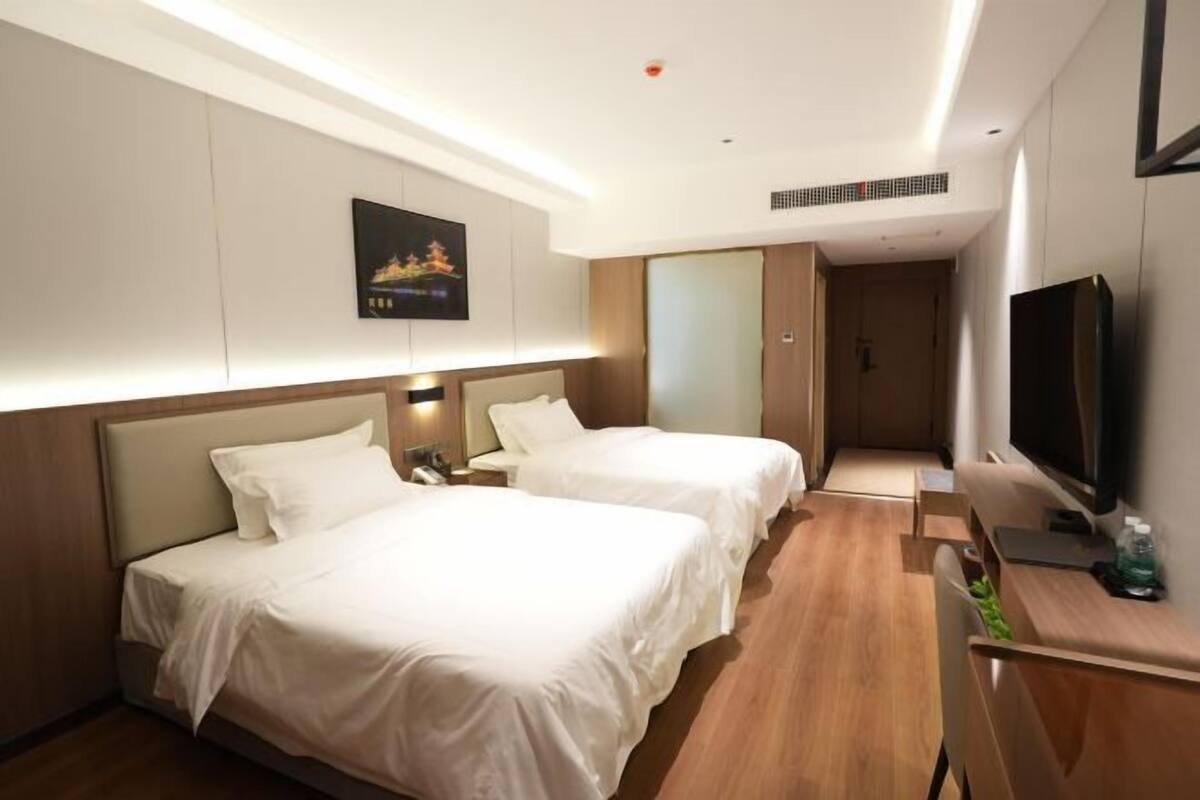 A hotel room with two beds, a TV, a desk, and a painting on the wall.