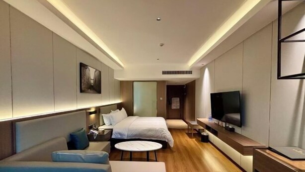 A modern hotel room with a bed, a sofa, a TV, and a small table. - Suining Linhai Hotel (Suining)