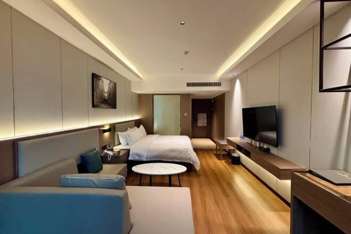 A modern hotel room with a bed, a sofa, a TV, and a small table.
