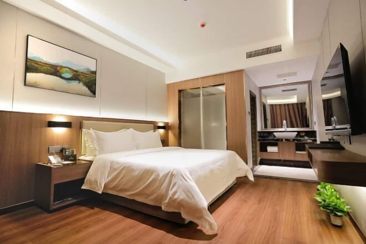 A hotel room with a bed, bedside table, lamp, artwork, and a view of the bathroom.