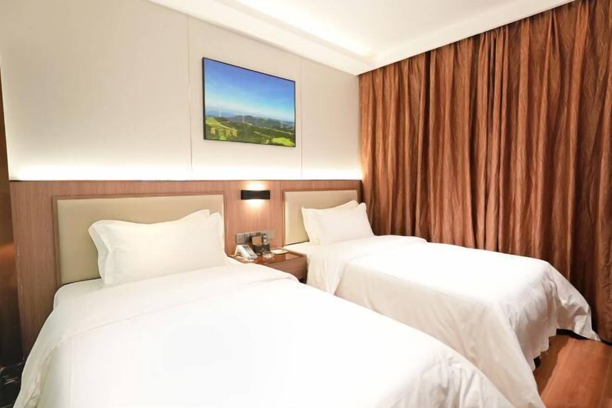 A hotel room with two beds, a nightstand with a phone, a painting of a landscape, and a large window with curtains.