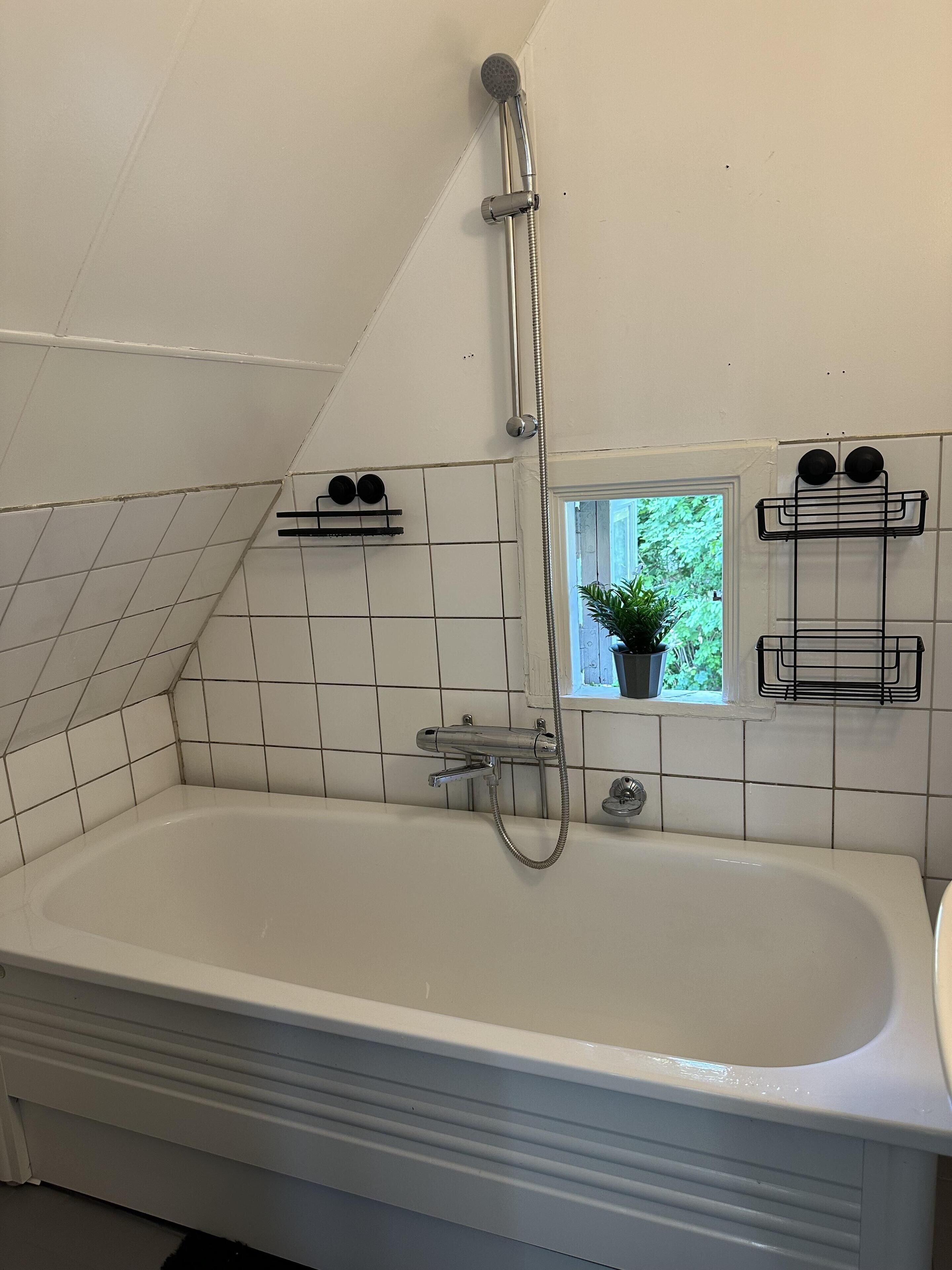 A bathroom with a bathtub, a shower, and a window with a view of greenery.