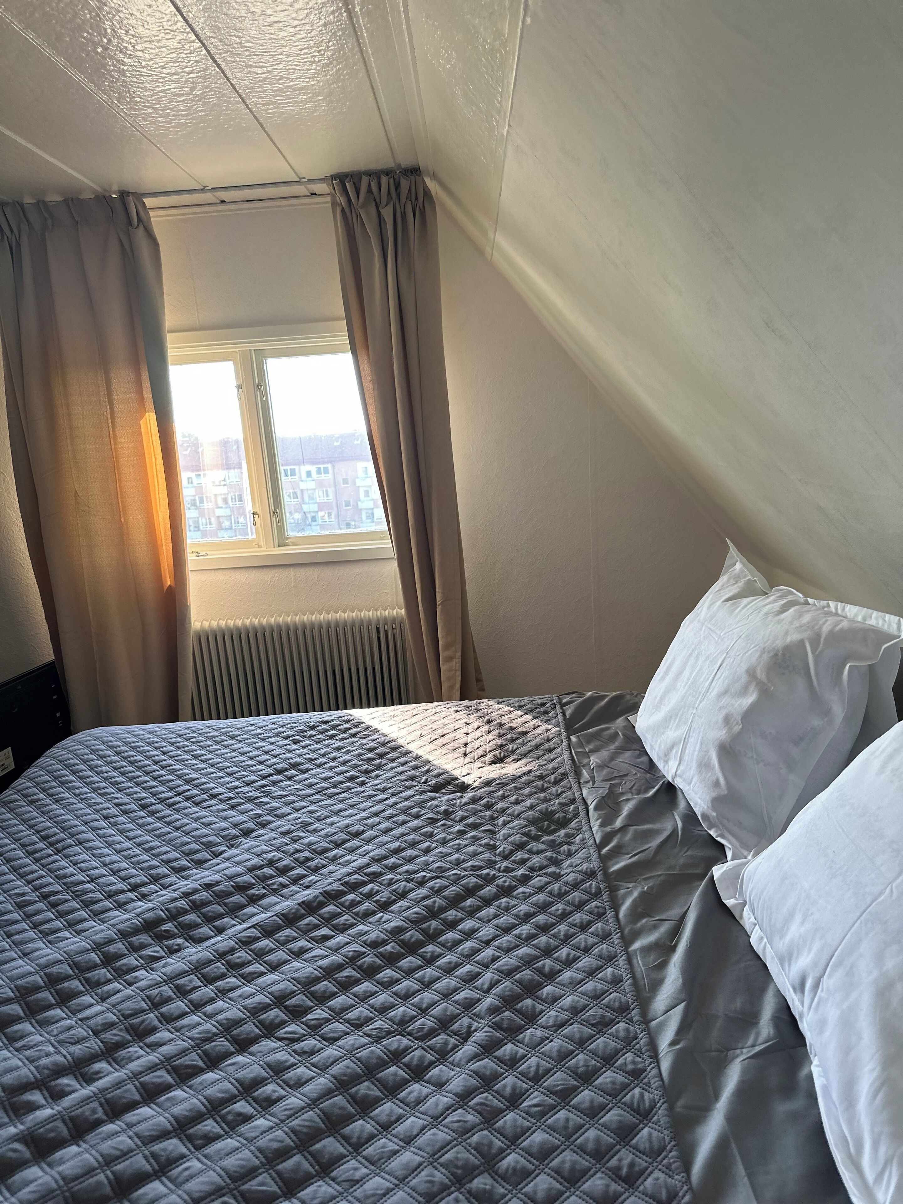 Un dormitorio con cama, almohadas blancas y una ventana con cortinas.