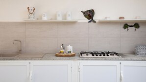 Una cucina con mobili bianchi, un piano di lavoro in granito, un lavello, un fornello a gas e diversi oggetti da cucina sugli scaffali.