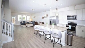 Une cuisine moderne avec des meubles blancs, des appareils en acier inoxydable et un îlot central doté de tabourets de bar.
