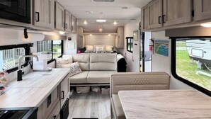 A compact RV interior with a kitchenette, a seating area, and a bed.