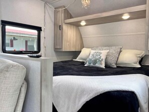 A compact bedroom with a bed, pillows, a window, and a small table.