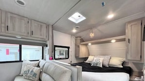 A compact RV interior with a bed, a sofa, and a small kitchenette area.