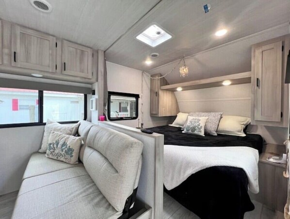 A compact RV interior with a bed, a sofa, and a small kitchenette area.