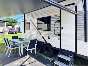 A white RV with a covered patio area, including a table and chairs.