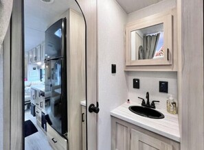 A compact kitchen with a refrigerator, a sink, and a mirror above the countertop.