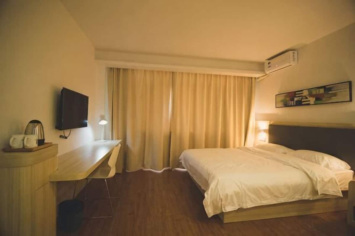 A hotel room with a bed, desk, chair, television, and curtains.