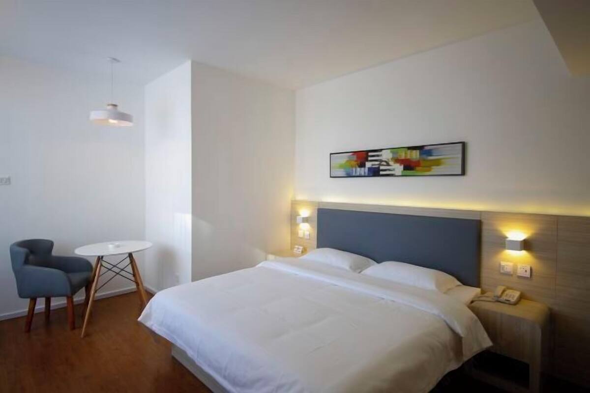 A hotel room with a bed, a small round table, a chair, and a wall-mounted artwork.